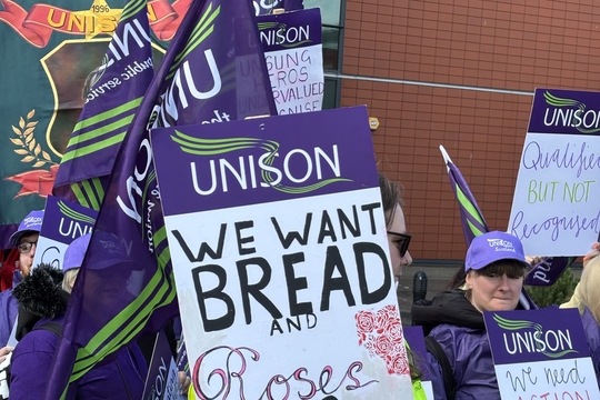 A Enable worker holds a Unison placard on a picket line reading "We want bread and roses too"