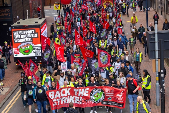 A group of Unite bin workers march with Sharon Graham in support of their long-running strike. At the head of the procession, Graham and the workers hold a long banner which reads 'back the strike'.