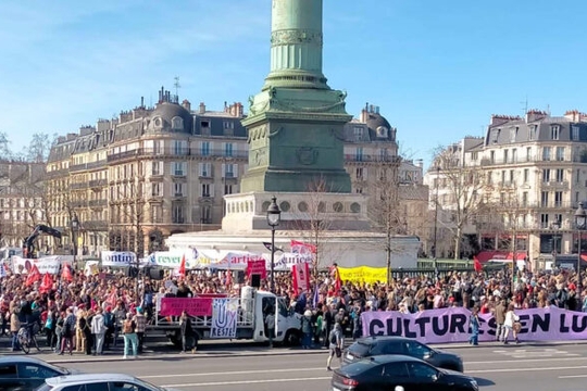 A large protest crowd gathered outside the Louvre, holding a pink banner that says "Cultures En Lutte" A large protest crowd gathered outside the Louvre, holding a pink banner that says "Cultures En Lutte"
