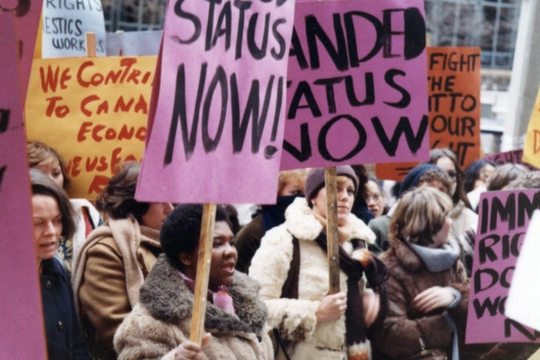 A photo of a protest by domestic workers in Canada in the 1980s. They hold placards saying "landed status now!"
