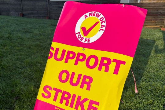 A vibrant pink and yellow protest sign on grass reads, "Support Our Strike" with a checkmark logo and "A New Deal for FE" above the UCU union logo.
